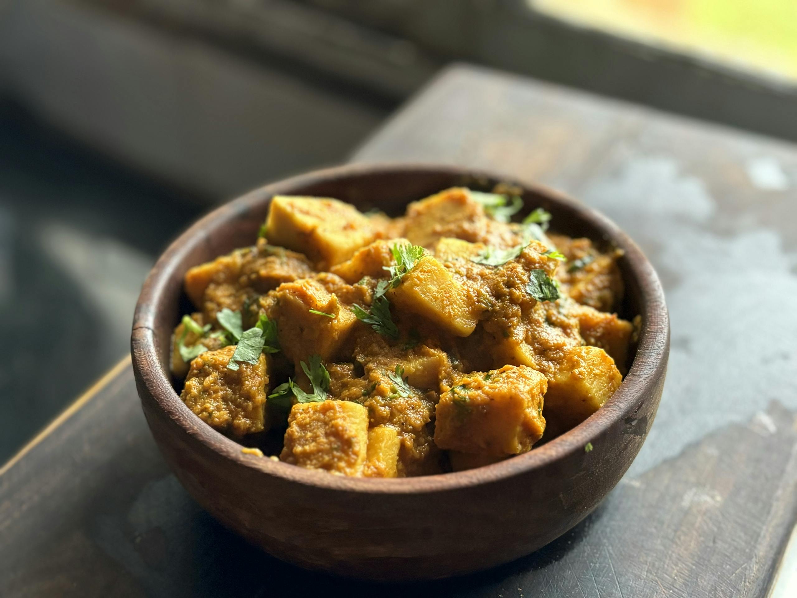 Delicious traditional Indian yam curry with cilantro served in a rustic bowl.